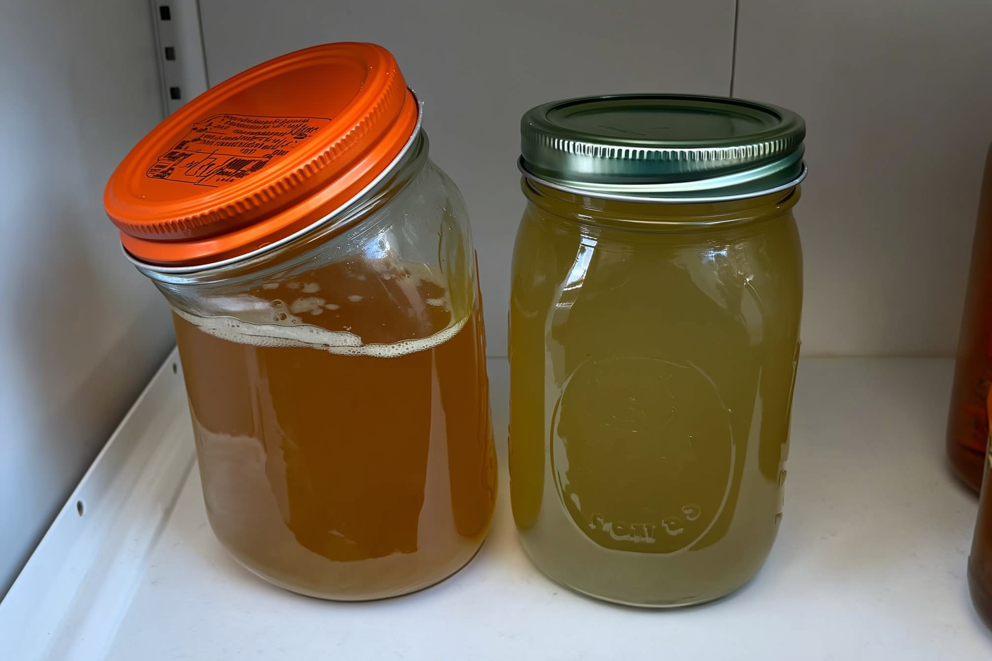 A Mason jar with a bulging lid and discolored liquid beside a properly sealed jar with a flat concave lid on a pantry shelf