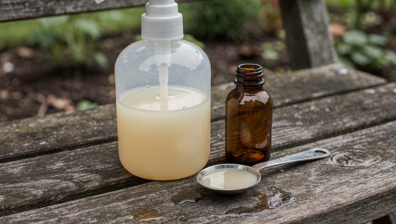 A pump sprayer being filled with a milky neem oil and water emulsion on a garden bench, a small bottle of concentrate and a measuring spoon beside it.