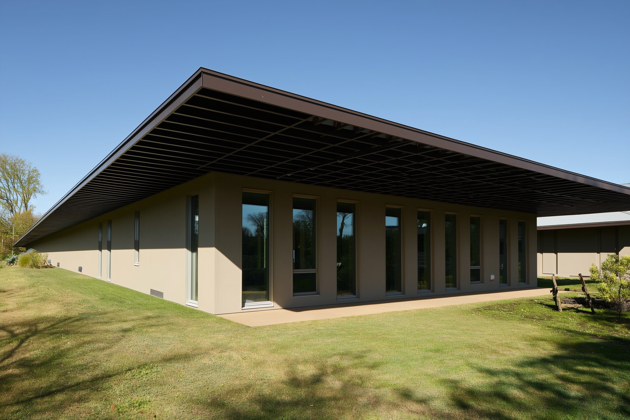 A deep horizontal roof overhang on a passive solar house casting a crisp shadow that shades the tall south-facing windows from high summer sun