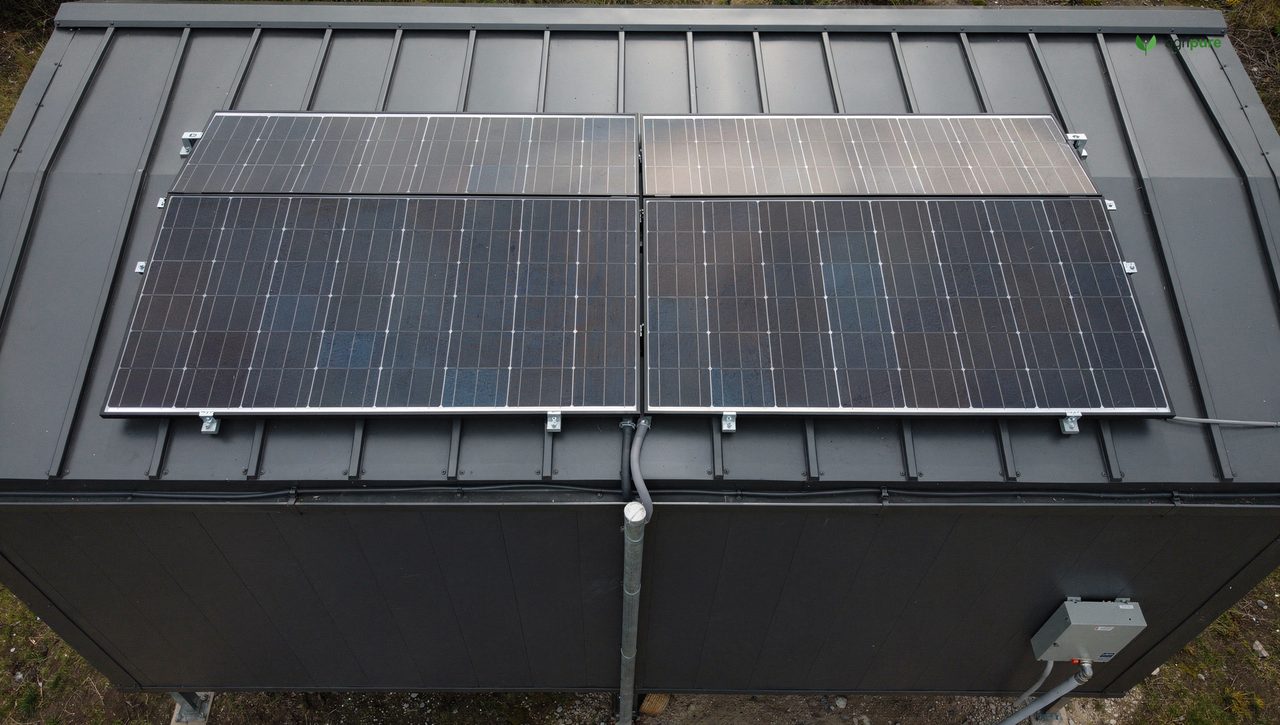 Two 300 W panels mounted flush on a tiny-house metal roof, conduit running to a side-wall electrical bay